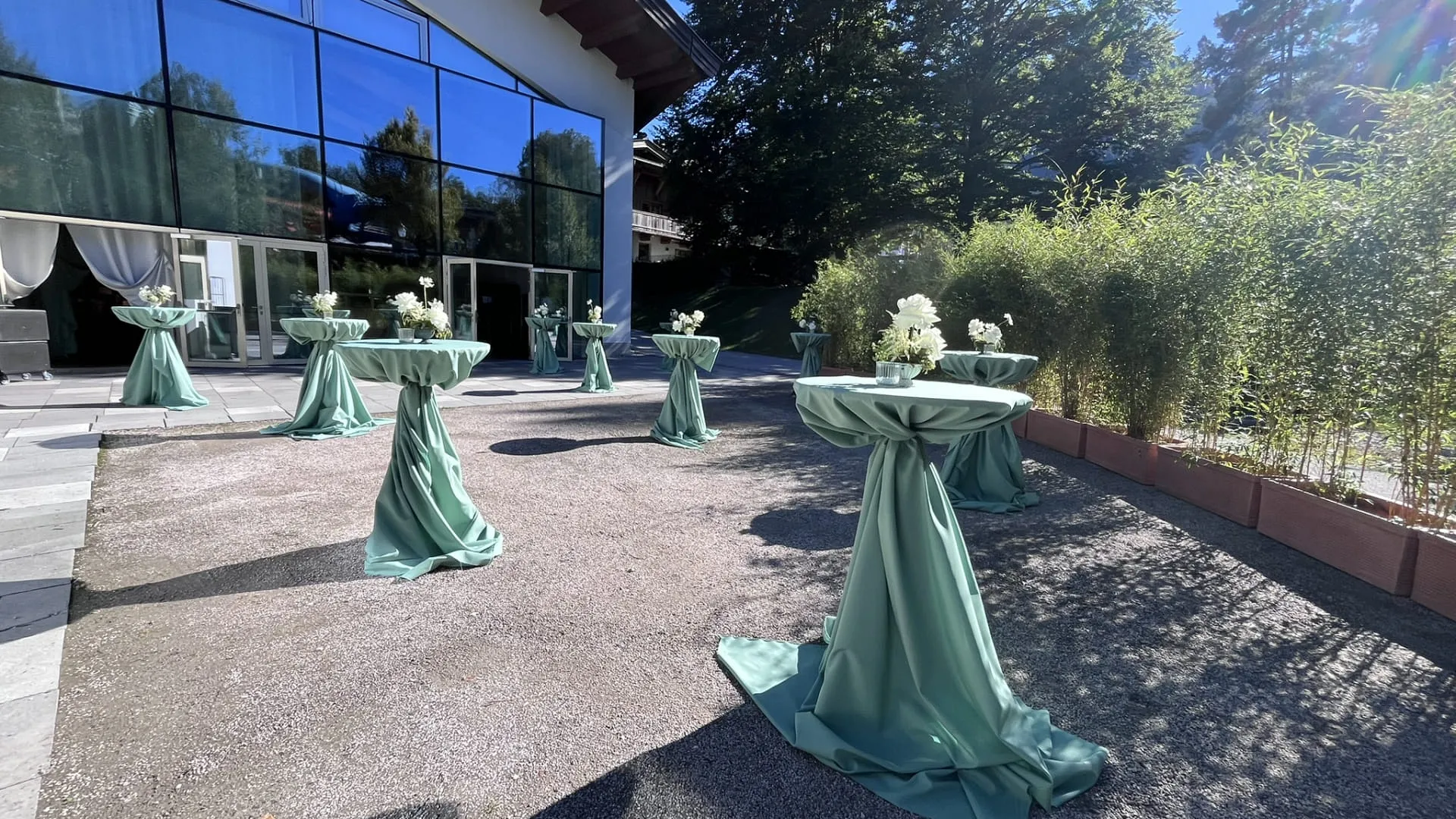 Hochtische, verkleidet mit dunkelgrünen Tischdecken und Blumenschmuck auf der grünen Terrasse für eine Hochzeit