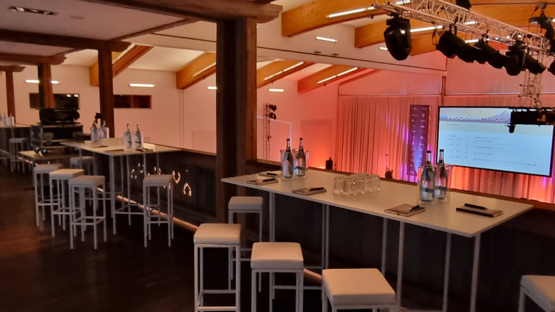 Moderne Eventlocation mit Stehtischen und Bildschirm.