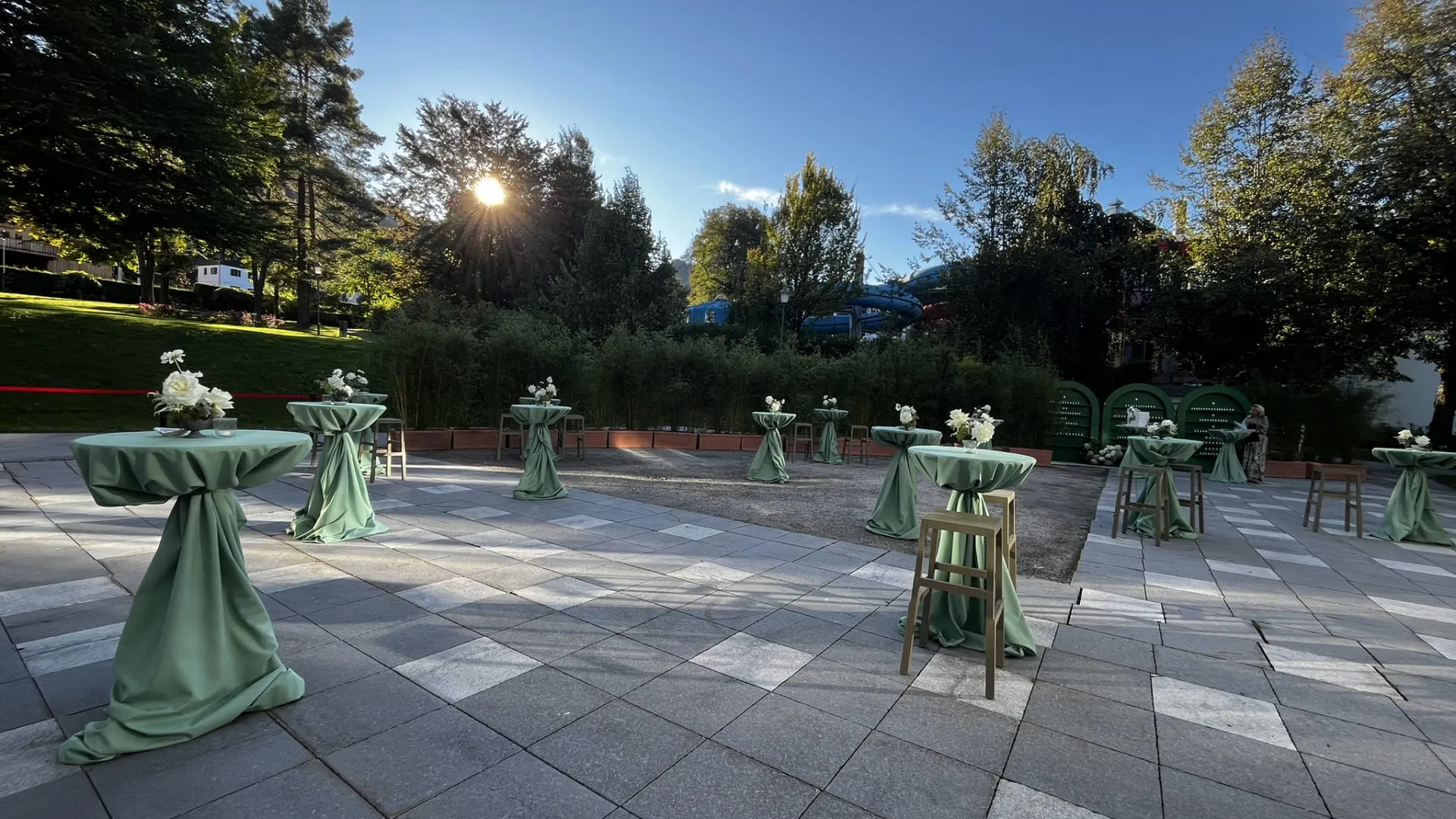 Gartenbereich mit Stehtischen und Sonnenuntergang im Hintergrund